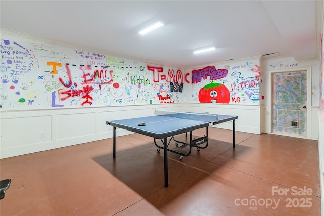 rec room with a decorative wall, wainscoting, and crown molding