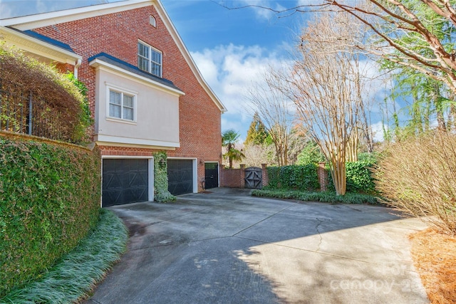 view of side of home featuring brick siding, driveway, a garage, and a gate