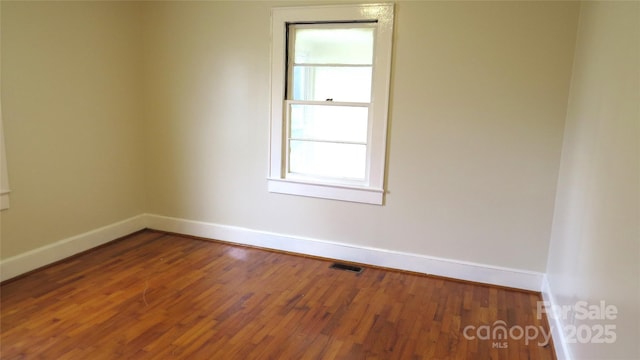 spare room featuring wood finished floors, visible vents, and baseboards
