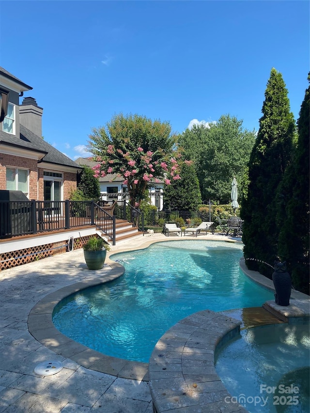 view of swimming pool featuring a pool with connected hot tub, a patio, a wooden deck, and fence