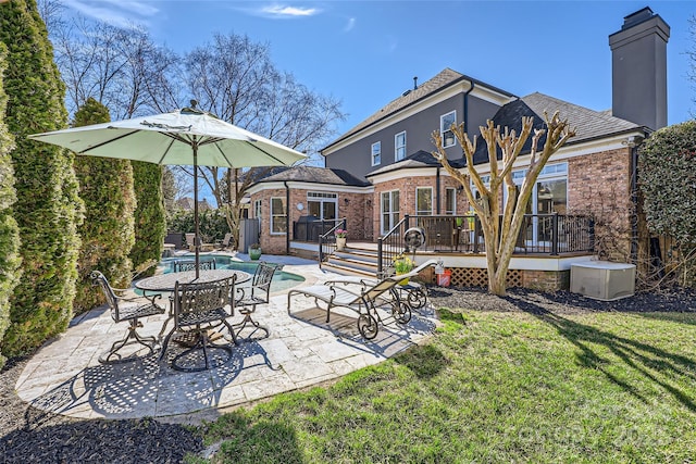 back of property featuring brick siding, a lawn, a patio area, an outdoor pool, and a wooden deck