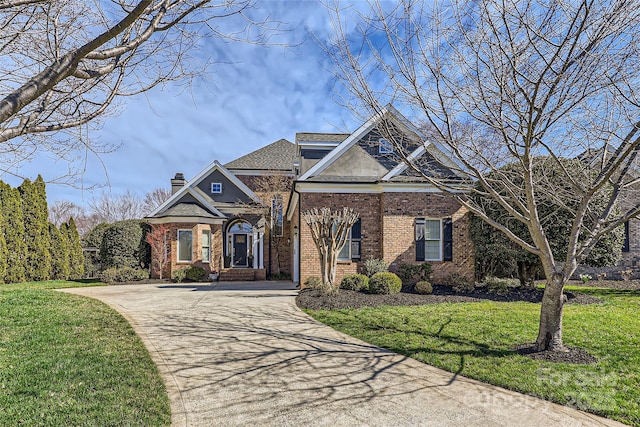 view of front of home with driveway, brick siding, a chimney, and a front yard