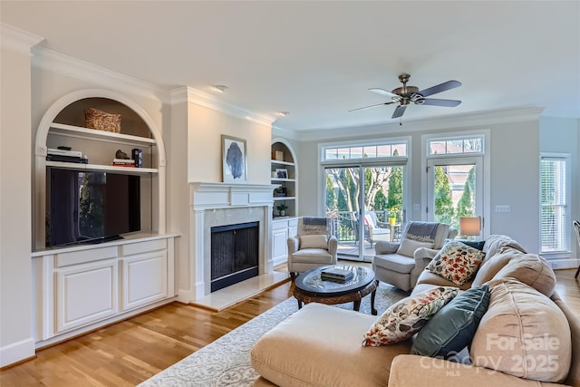 living area featuring built in shelves, crown molding, plenty of natural light, and light wood finished floors