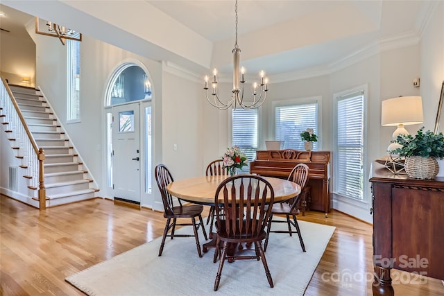 dining area featuring light wood-style flooring, a tray ceiling, a chandelier, and ornamental molding