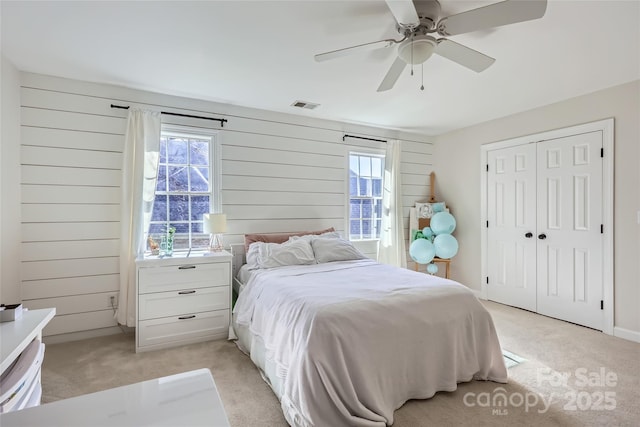 bedroom featuring a closet, visible vents, light carpet, wood walls, and ceiling fan