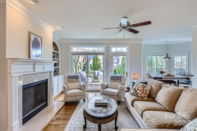 living room featuring a ceiling fan, ornamental molding, wood finished floors, built in shelves, and a high end fireplace