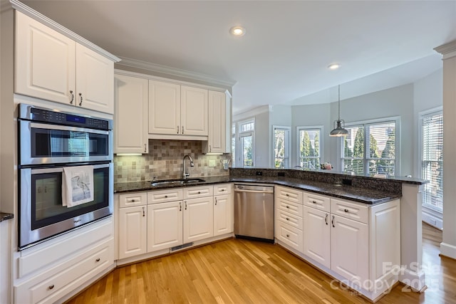 kitchen featuring stainless steel appliances, decorative backsplash, white cabinetry, a sink, and a peninsula