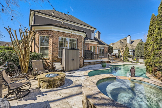 back of house with an outdoor fire pit, a patio, a wooden deck, a pool with connected hot tub, and brick siding