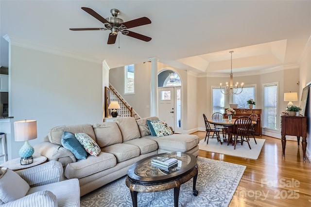 living room featuring light wood finished floors, stairs, a tray ceiling, and crown molding