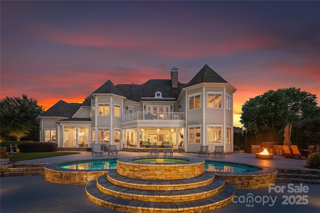 rear view of property with a pool with connected hot tub, a patio, a fire pit, a balcony, and a chimney