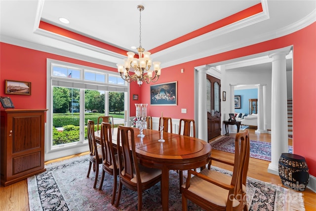 dining area featuring a tray ceiling, light wood-style floors, an inviting chandelier, and decorative columns