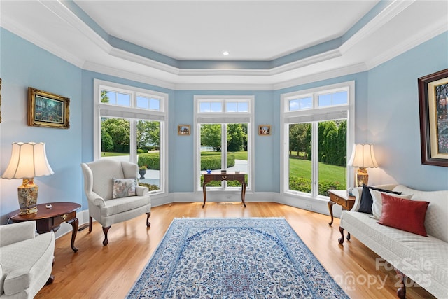 sitting room with baseboards, a raised ceiling, light wood-style floors, and ornamental molding