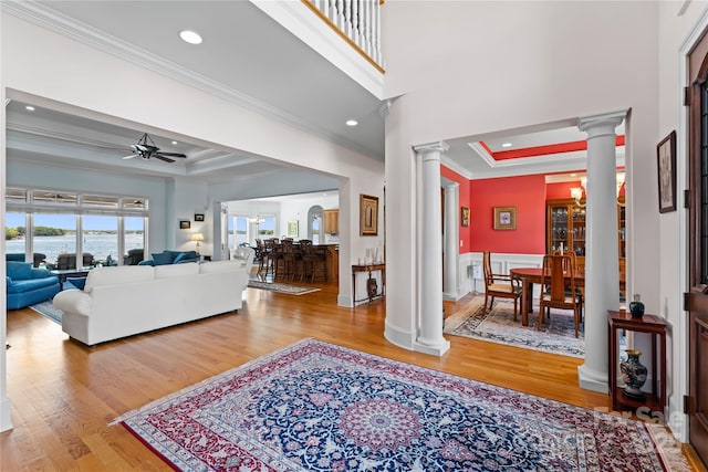 living area with crown molding, a raised ceiling, ornate columns, and wood finished floors