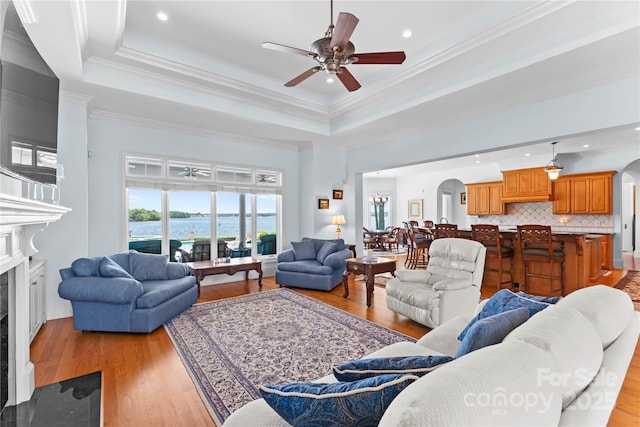 living area featuring arched walkways, a ceiling fan, and a tray ceiling