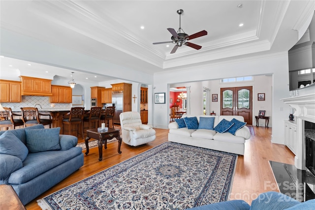 living room with ceiling fan, ornamental molding, light wood-style flooring, a fireplace, and a raised ceiling