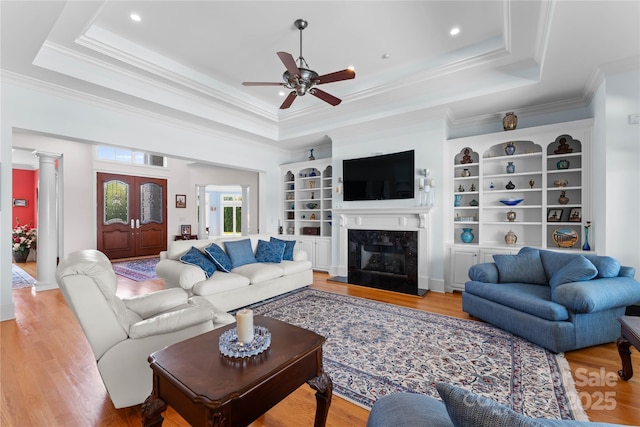 living area with a raised ceiling, light wood-style floors, ceiling fan, and a fireplace