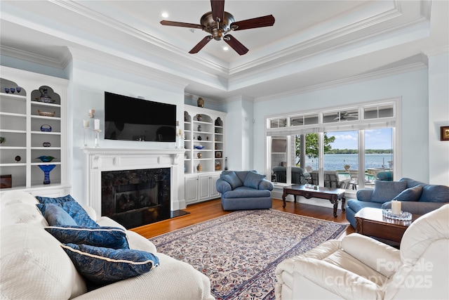 living room featuring a premium fireplace, wood finished floors, a raised ceiling, and ceiling fan