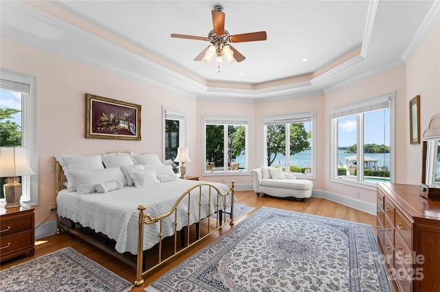 bedroom featuring light wood-style flooring, a ceiling fan, ornamental molding, a tray ceiling, and baseboards