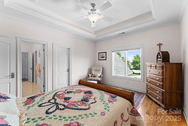 bedroom featuring visible vents, ceiling fan, light wood-type flooring, ornamental molding, and a raised ceiling