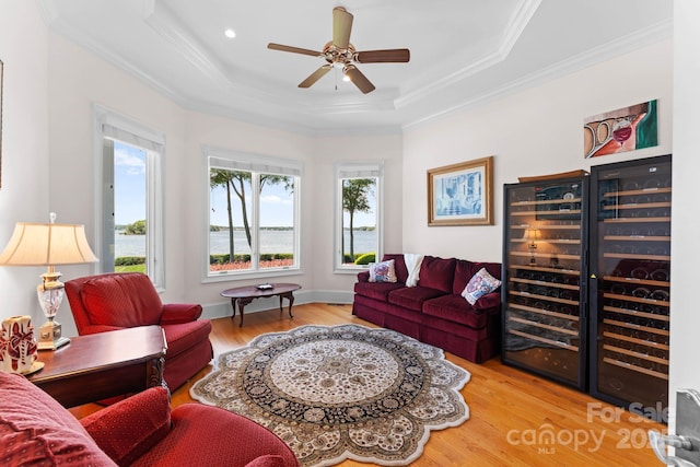 living area featuring a raised ceiling, ornamental molding, wood finished floors, baseboards, and ceiling fan