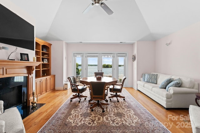 dining space with light wood finished floors, a fireplace, a ceiling fan, and a water view