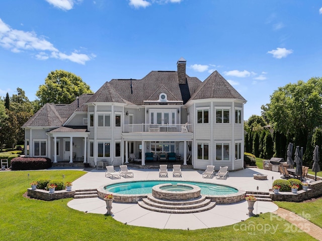 rear view of house with a pool with connected hot tub, a chimney, a yard, a balcony, and a patio area