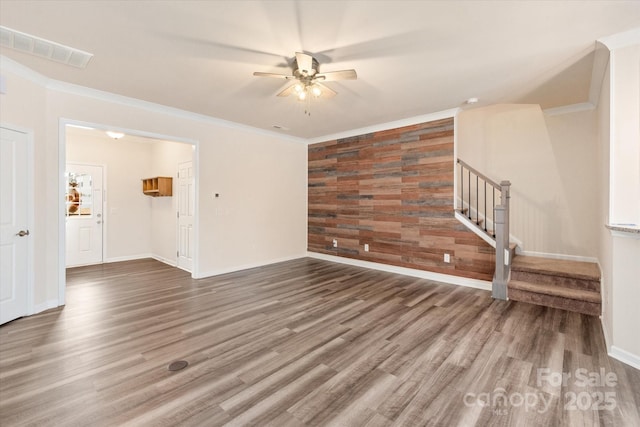 unfurnished living room with visible vents, an accent wall, wood finished floors, stairs, and crown molding