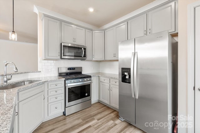 kitchen featuring a sink, appliances with stainless steel finishes, light wood-type flooring, decorative backsplash, and light stone countertops