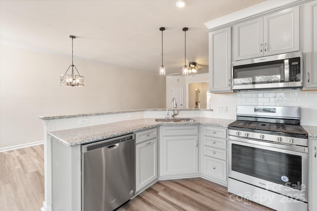 kitchen featuring tasteful backsplash, appliances with stainless steel finishes, a peninsula, light wood-type flooring, and a sink