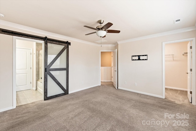 unfurnished bedroom with a barn door, baseboards, carpet, a spacious closet, and crown molding