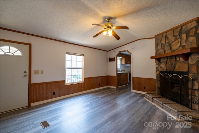 unfurnished living room featuring a textured ceiling, wood finished floors, visible vents, vaulted ceiling, and wainscoting