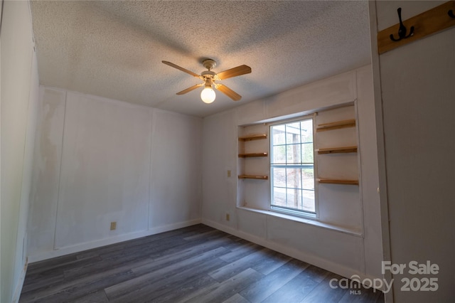 unfurnished room with a textured ceiling, dark wood finished floors, a ceiling fan, and a decorative wall