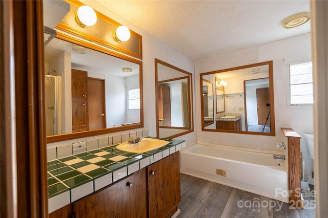 bathroom featuring a garden tub, a textured ceiling, wood finished floors, and vanity