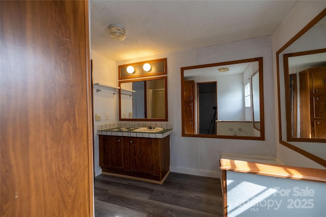 bathroom with a textured ceiling, baseboards, wood finished floors, and vanity