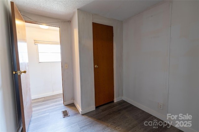 interior space with visible vents, a textured ceiling, baseboards, and wood finished floors