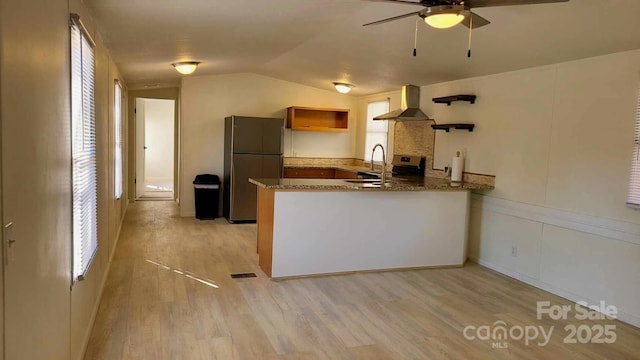 kitchen featuring light wood-style flooring, a peninsula, wall chimney range hood, freestanding refrigerator, and open shelves