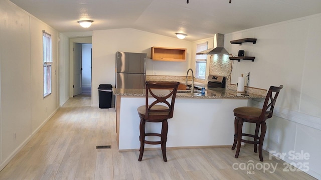 kitchen with open shelves, appliances with stainless steel finishes, a sink, wall chimney range hood, and a peninsula