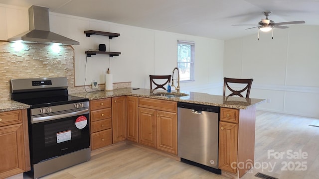 kitchen featuring a peninsula, stainless steel appliances, wall chimney range hood, open shelves, and a sink