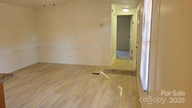 spare room featuring visible vents, a decorative wall, and wood finished floors