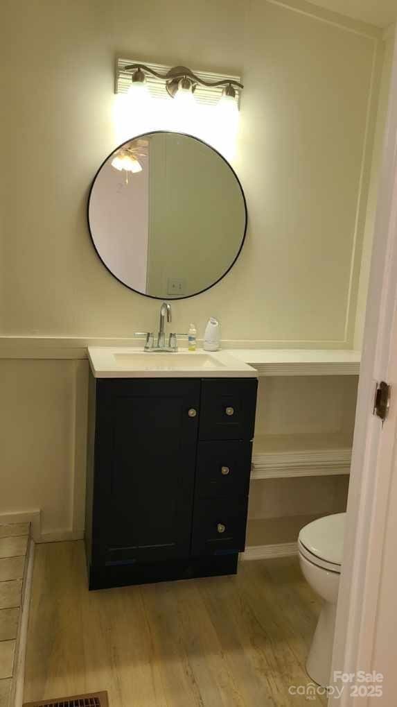 half bathroom with toilet, wood finished floors, and vanity