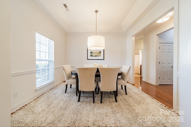 dining room with baseboards, visible vents, a raised ceiling, wood finished floors, and crown molding