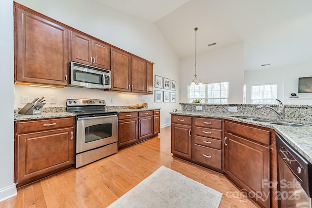 kitchen featuring pendant lighting, light wood finished floors, stainless steel appliances, vaulted ceiling, and a sink