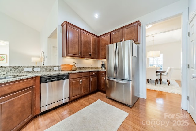 kitchen featuring light stone counters, light wood-style flooring, appliances with stainless steel finishes, a sink, and vaulted ceiling