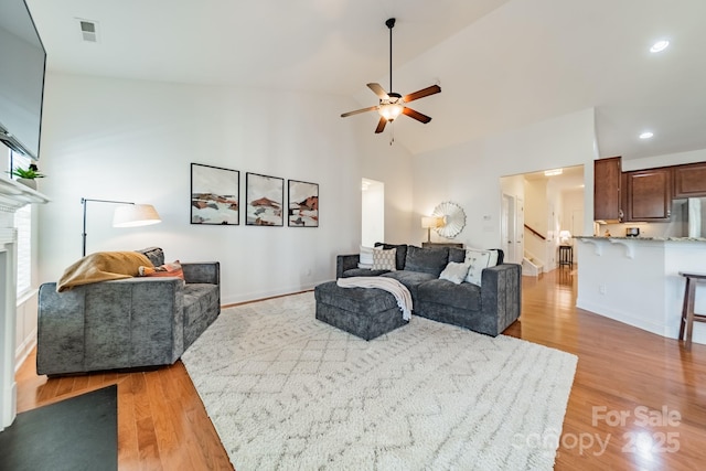 living room featuring a fireplace, light wood finished floors, visible vents, stairway, and high vaulted ceiling