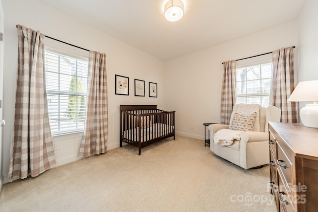 bedroom with baseboards, a crib, and light colored carpet