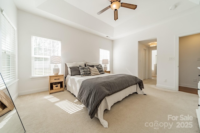 bedroom featuring a ceiling fan, a raised ceiling, light colored carpet, and baseboards