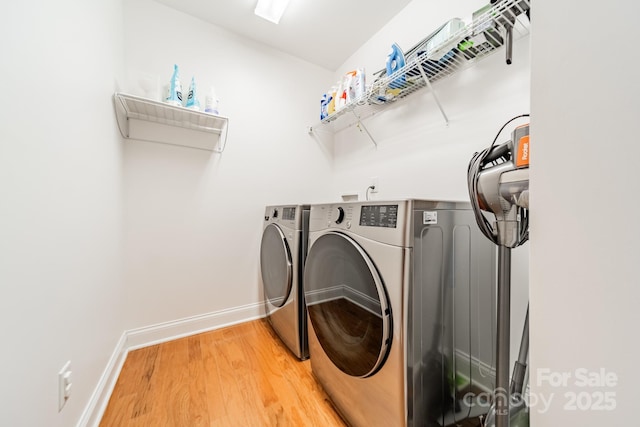 clothes washing area with laundry area, baseboards, wood finished floors, and washing machine and clothes dryer