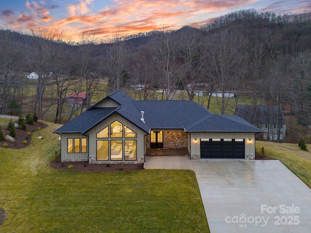 view of front of home featuring a garage, a shingled roof, stone siding, concrete driveway, and a front lawn