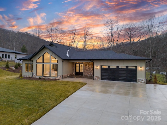 view of front of home with a garage, a lawn, concrete driveway, stone siding, and board and batten siding