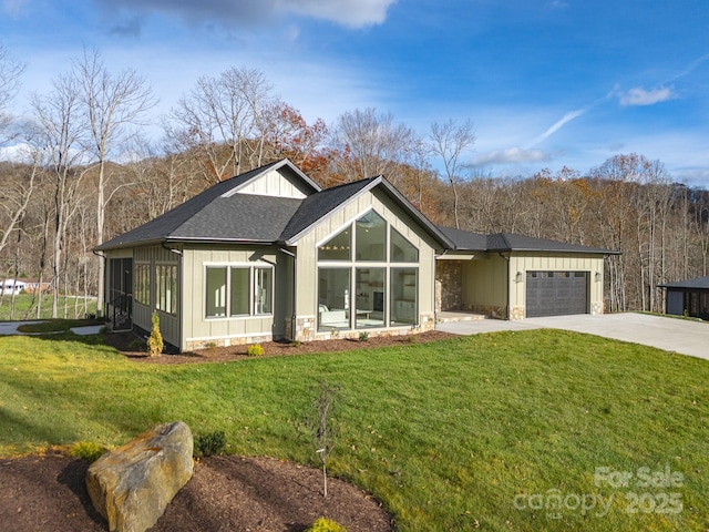 view of front of house with an attached garage, a shingled roof, stone siding, driveway, and a front lawn